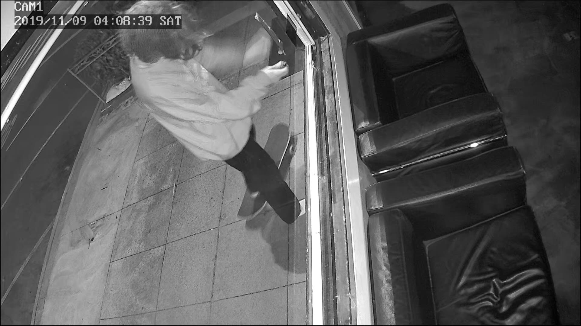 In surveillance footage, a man is seen riding up on a skateboard, attaching something on the front window, igniting a stick and then taking off before it explodes.