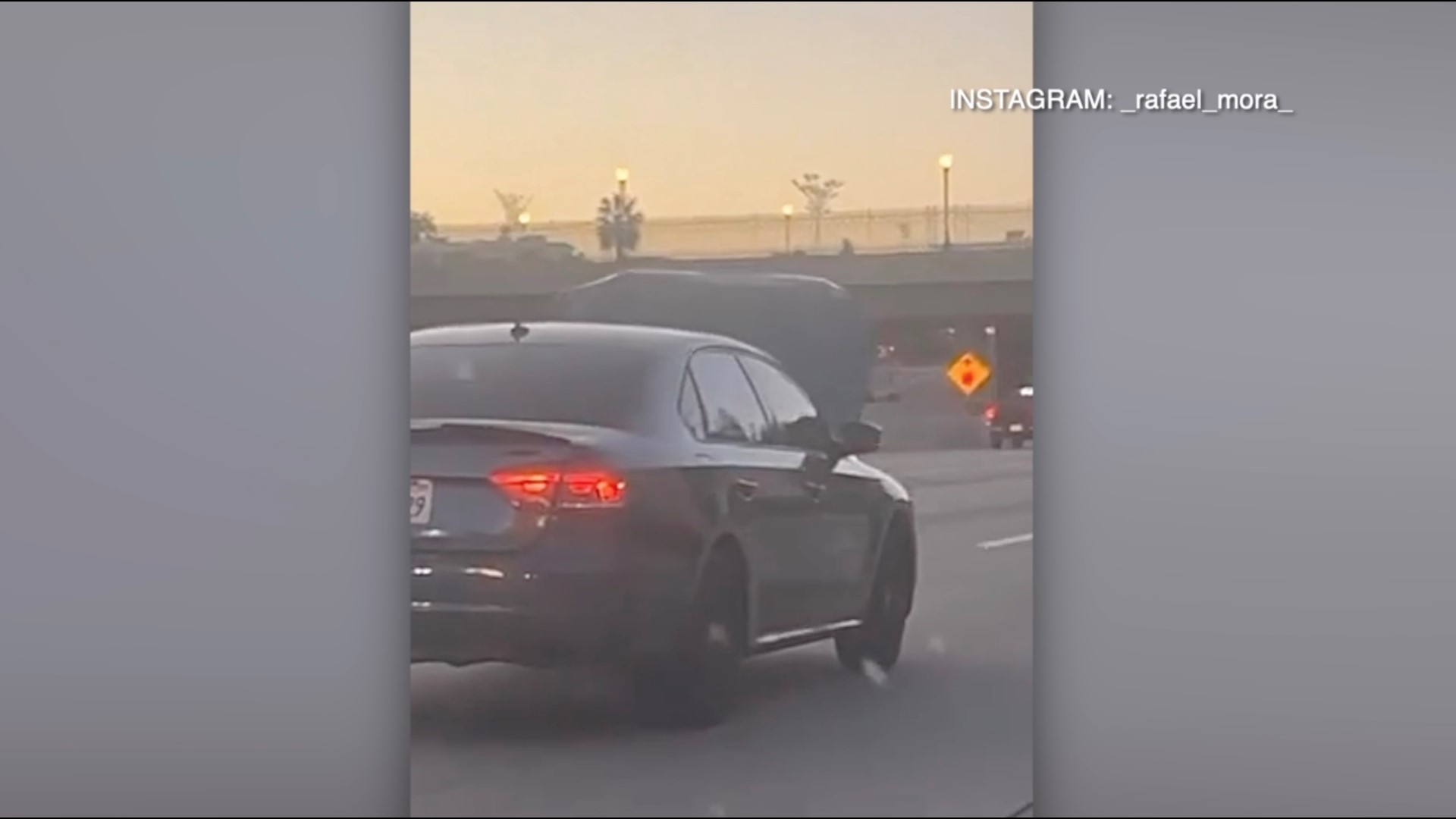 A person was recorded driving on the freeway with their engine's hood unlatched, blocking their entire front windshield.